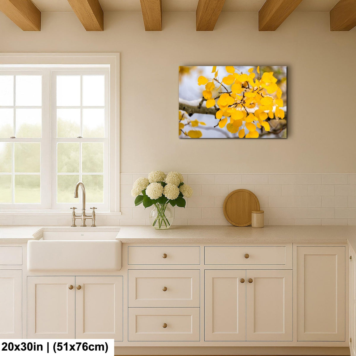 a kitchen with a white sink, a vase of white flowers, and a framed picture of yellow leaves hanging on the wall.