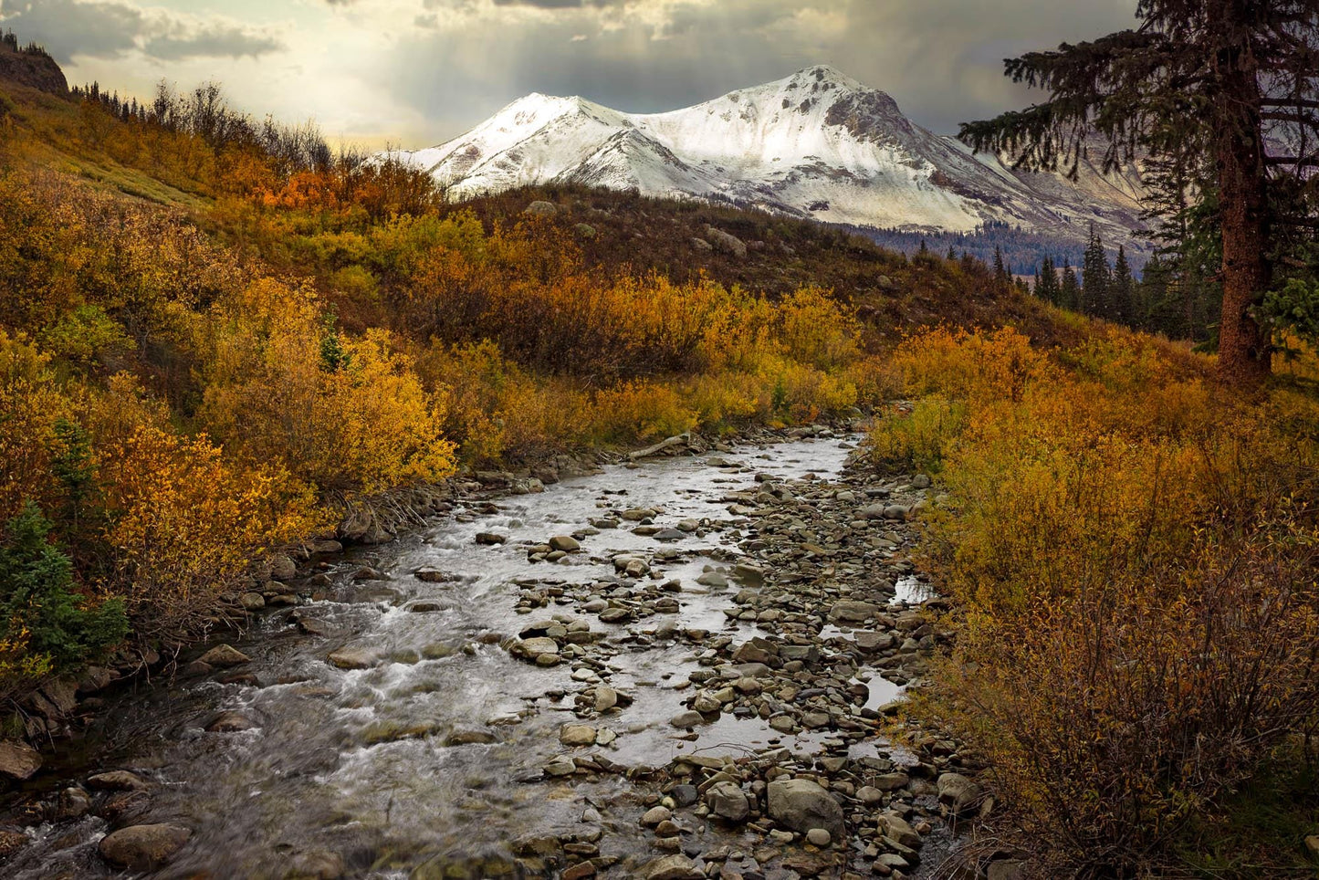 Colorado fall landscape photo of snowy mountain peaks rising above a stream, with autumn colors. Available in fine art paper, canvas, metal and acrylic.