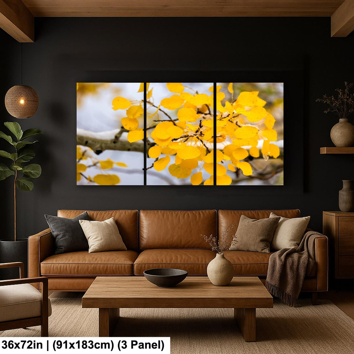 A modern living room with a large, three-panel painting of a tree branch with yellow leaves hanging on the wall. The painting is framed in black and is the focal point of the room. The room has a brown leather sofa, a wooden coffee table, and various decorative elements such as a potted plant, vases, and a bowl.