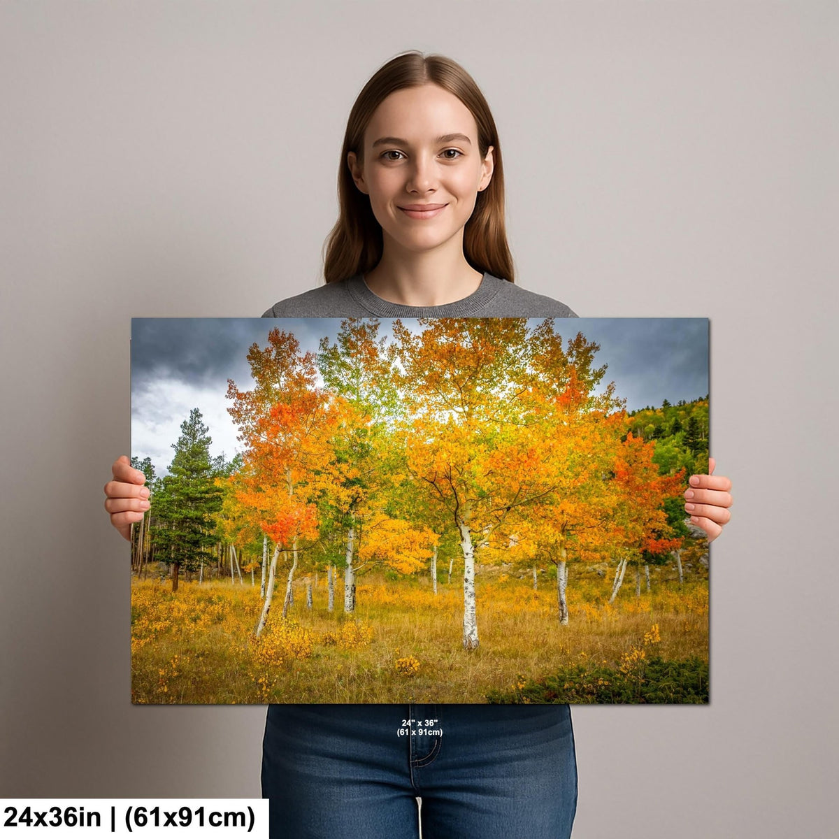 A woman is holding up a large canvas print of a vibrant autumn landscape featuring a forest of trees with orange and yellow foliage.