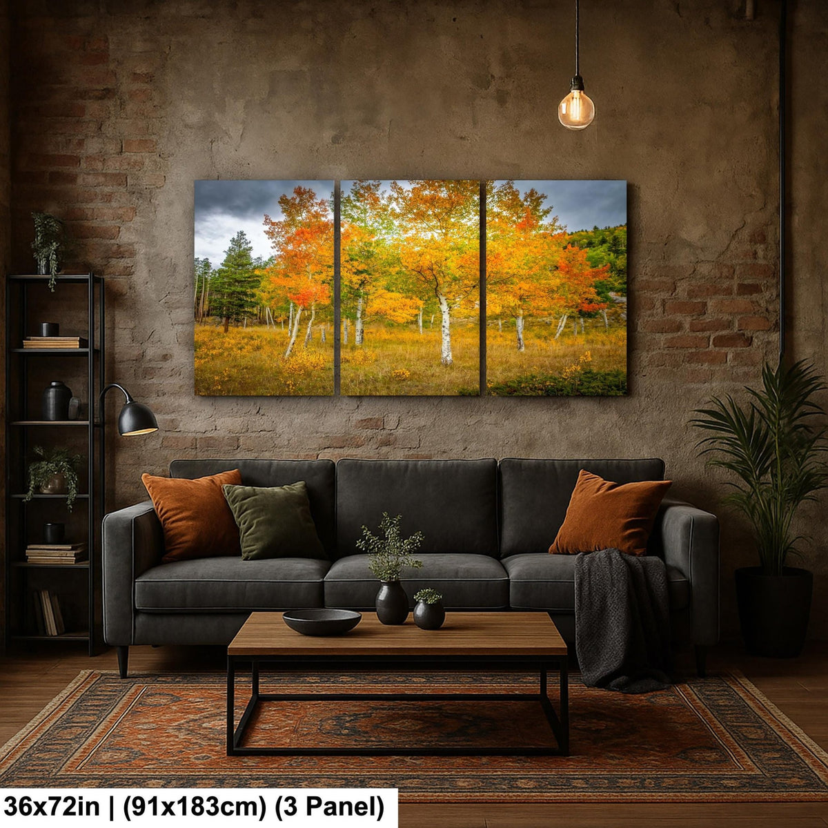 The image is a modern living room with a large, three-panel landscape painting hanging on the brick wall above a gray sofa. The painting depicts a scenic autumn forest with vibrant orange and yellow foliage. The room also includes a coffee table, a potted plant, and a bookshelf, creating a cozy and inviting atmosphere.