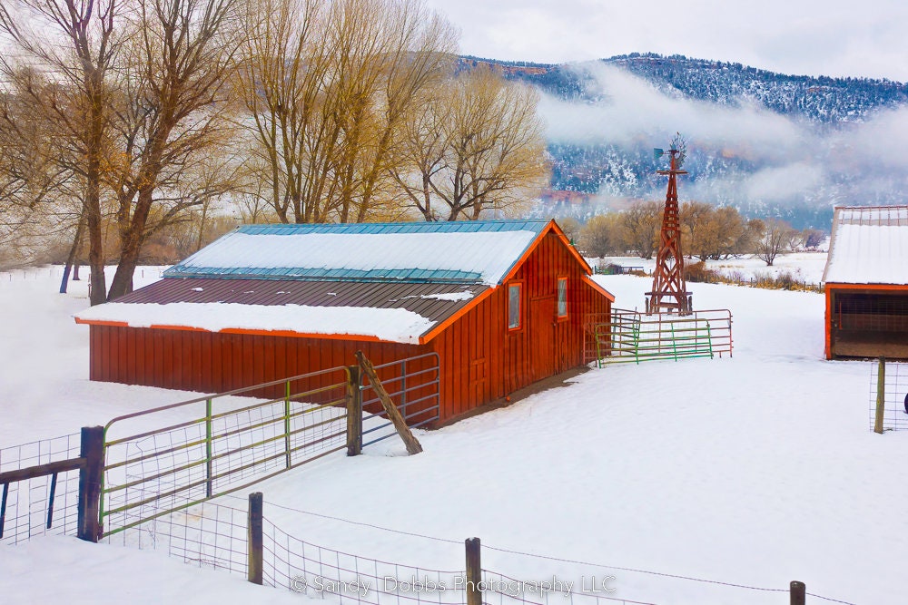 Rustic red barn in snowy winter landscape, with autumn trees in background. Available in prints or canvases.