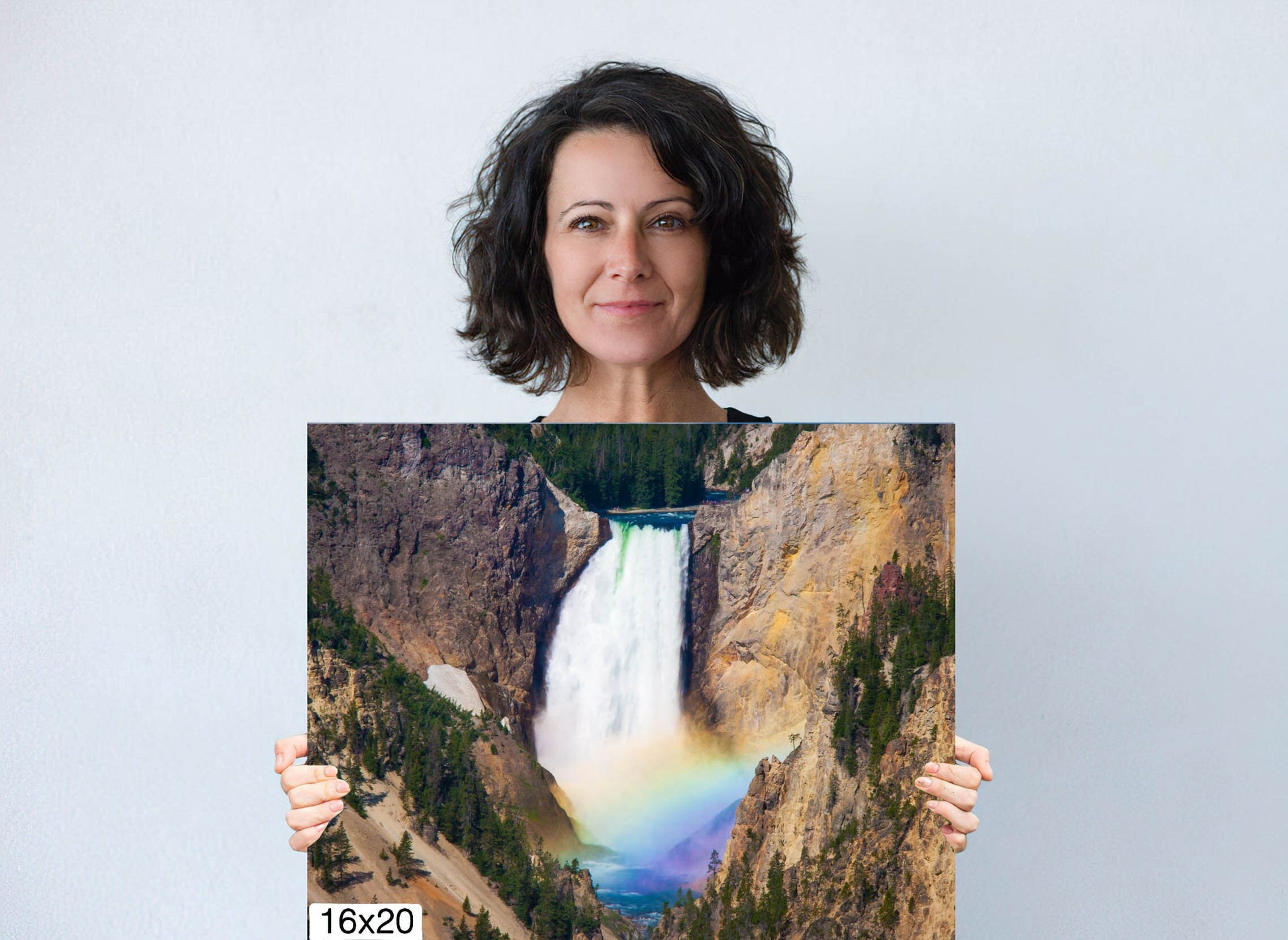 Woman holding 16x20 canvas size of Lower. Falls of the Yellowstone River in Yellowstone National Park with beautiful rainbow at the base of the falls. Canvas wall art decor for home or office.