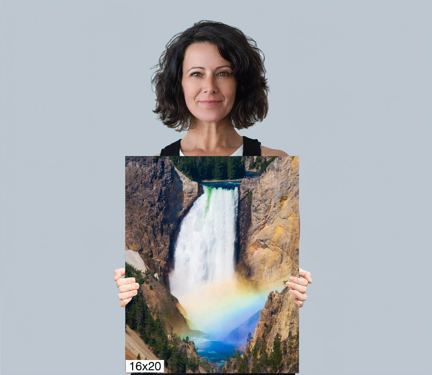 Woman holding 16x20 canvas size of Lower. Falls of the Yellowstone River in Yellowstone National Park with beautiful rainbow at the base of the falls. Canvas wall art decor for home or office.