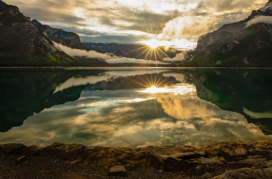 Beautiful sunrise with a starburst of the sun rising and reflecting into Lake Minnewanka in Banff National Park in Canada.