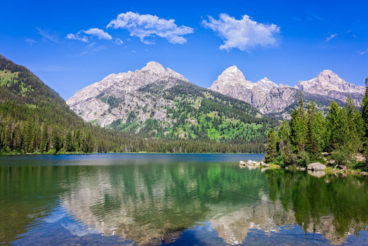 Beautiful mountain lake reflection in Grand Teton National Park. Taggart Lake with bright blue skies and still water, reflecting green in the water. Available in fine art photo prints, canvases, acrylic and metal.